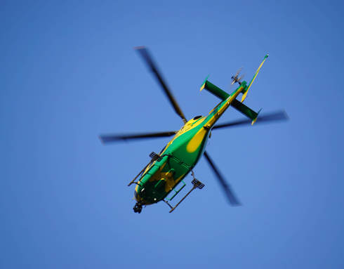 The yellow and green helicopter in flight against a blue sky.