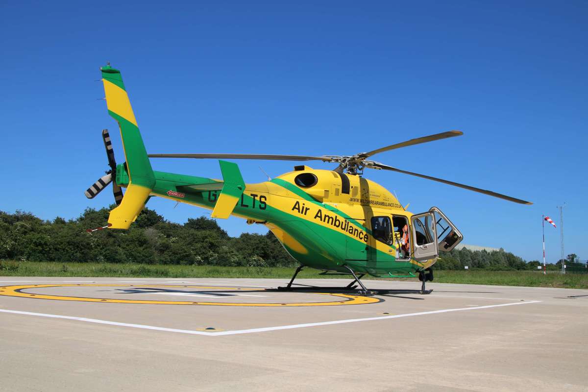 The yellow and green helicopter landed on the helipad against a blue sky.