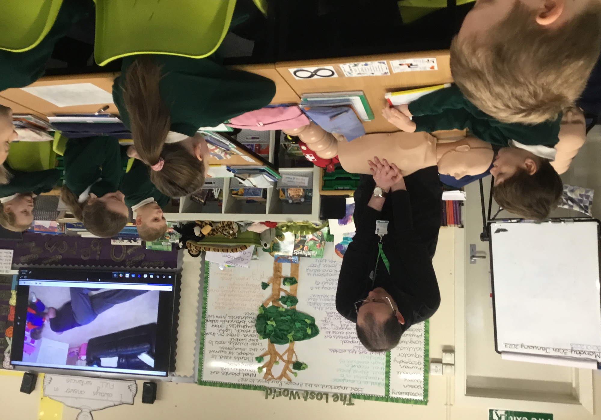 A man performing CPR on a manikin, with school children watching on