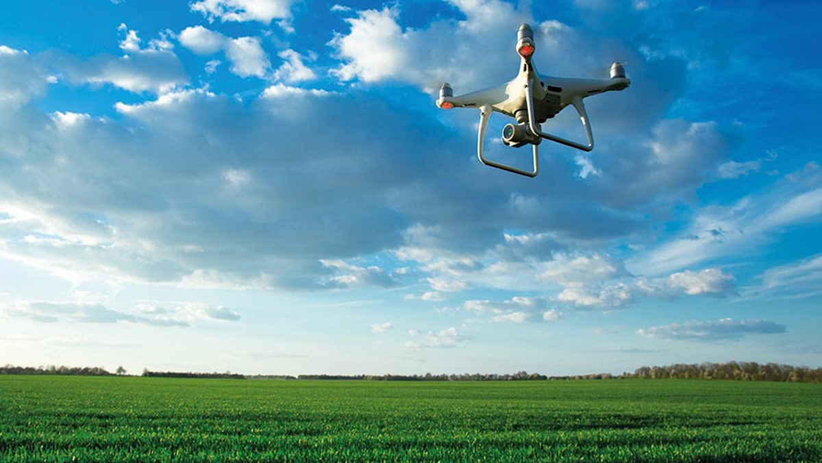 A drone flying in the blue skies over a green field