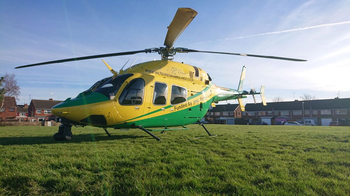 A yellow and green helicopter landed on a green in Swindon, with houses behind