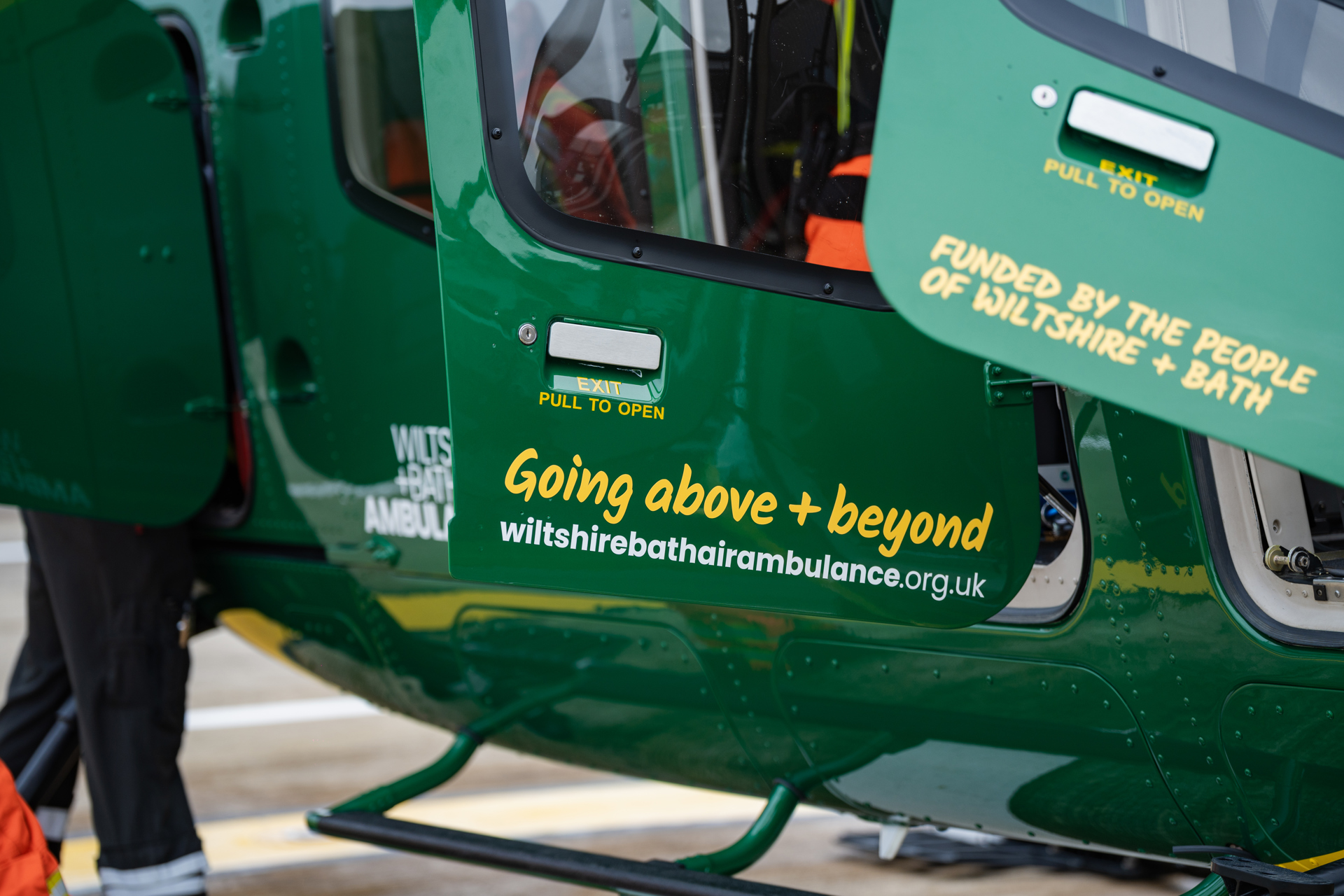 Yellow text with going above + beyond and funded by the people of wiltshire + bath on the doors of a green helicopter