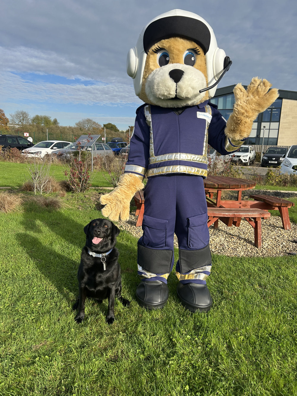 Air Ambulance pilot mascot standing with a black Labrador outside the airbase