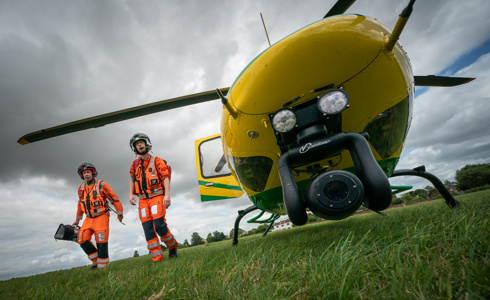 The nose of a yellow and green aircraft with two paramedics wearing orange flight suits walking alongside